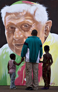 Deux générations devant le portrait peint du Pape Benoît XVI, dont la calotte et la chasuble représentent le drapeau du Cameroun à Yaoundé, le 15 mars 2009. (Photo : Reuters)
